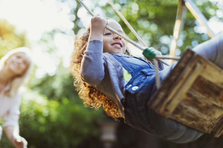 Mum pushing daughter on a swing in the summer